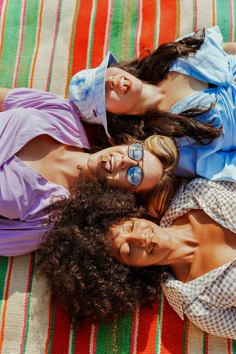 Three women laying on a blanket with Kanna Gum in their mouths