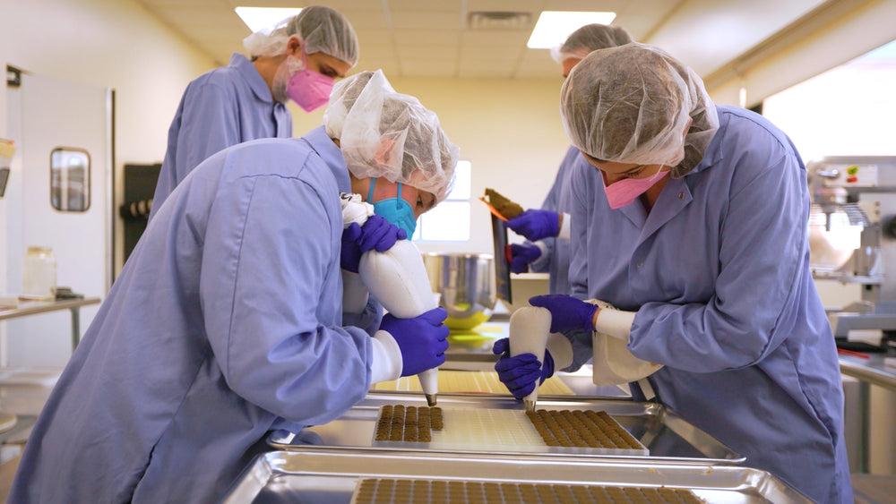 People in a food production facility wearing blue uniforms and hairnets.