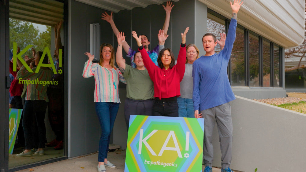 Group of people celebrating with raised hands in front of a building with 'KA!' branding.